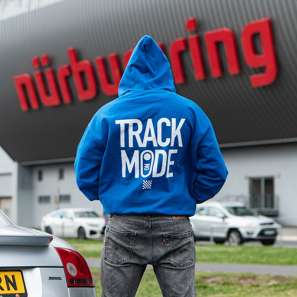 Person wearing a blue hoodie with 'Track Mode' text in front of a building with 'nurburgring' branding.